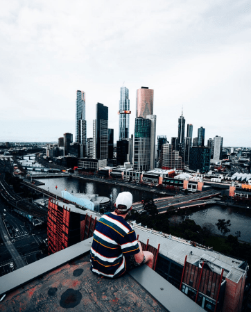 man-in-white-red-and-black-striped-shirt-sitting-on-the-edge-of-a-building-looking